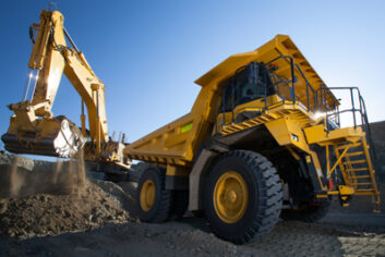 clean image of yellow excavator loading soil on a truck at mine back lit